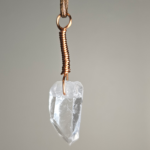 A quartz crystal pendant drilled that has a copper wire wrapped bail.