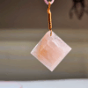 A pink rose quartz faceted pendant with a copper wire wrapped bail.