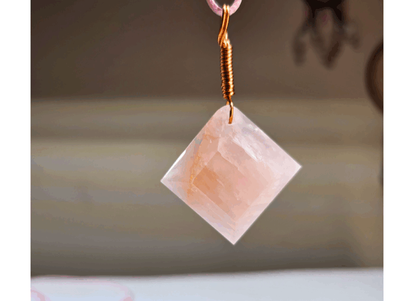 A pink rose quartz faceted pendant with a copper wire wrapped bail.