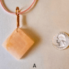 A pink rose quartz faceted pendant with a copper wire wrapped bail, and a quarter for size comparison. Labeled A.