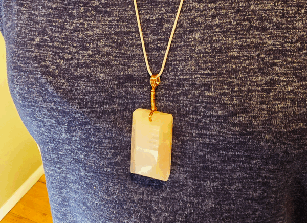 A pink rose quartz faceted pendant with a copper wire wrapped bail being worn.