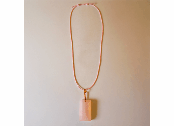 A pink rose quartz faceted pendant with a copper wire wrapped bail, with full display of an adjustable pink wax cord necklace attached.