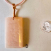 A pink rose quartz faceted pendant with a copper wire wrapped bail, and a quarter for size comparison. Labeled D.